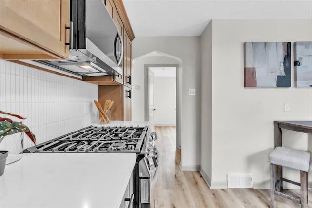 kitchen featuring visible vents, baseboards, arched walkways, light wood finished floors, and stainless steel appliances