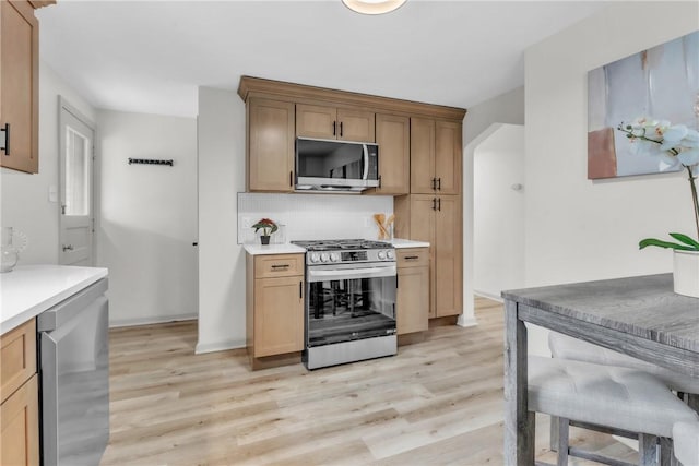 kitchen featuring stainless steel appliances, light wood finished floors, light countertops, and backsplash