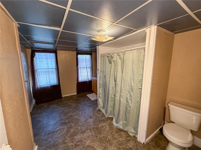bathroom featuring toilet, curtained shower, and baseboards