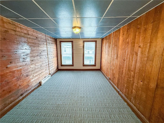 carpeted empty room with wooden walls, baseboard heating, and baseboards