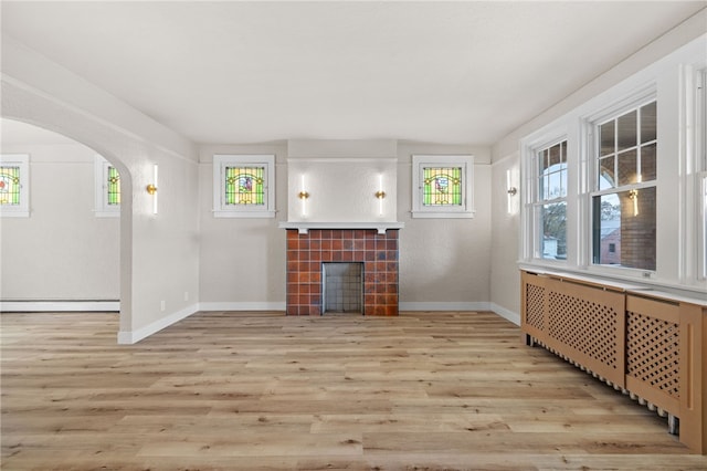 unfurnished living room with a baseboard heating unit, baseboards, a tiled fireplace, radiator heating unit, and wood finished floors