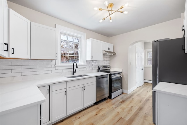 kitchen featuring arched walkways, a notable chandelier, a sink, appliances with stainless steel finishes, and under cabinet range hood