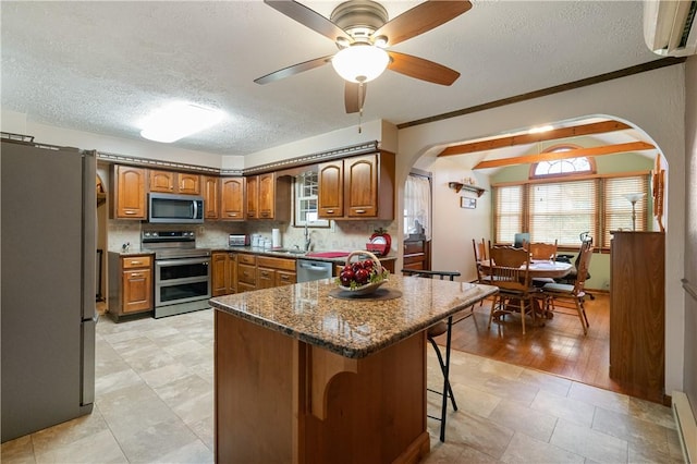 kitchen with brown cabinetry, arched walkways, a textured ceiling, a wall mounted AC, and stainless steel appliances