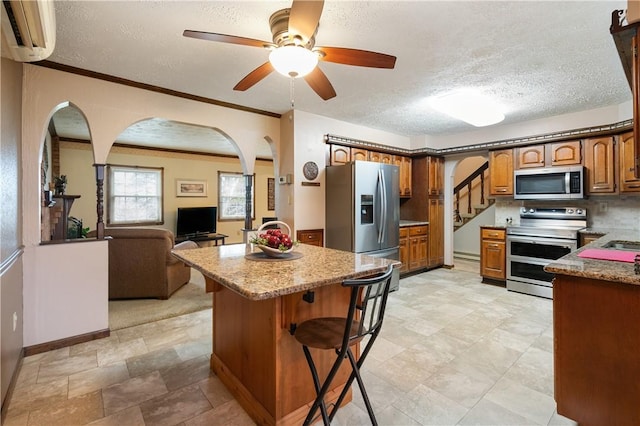 kitchen with brown cabinetry, arched walkways, a textured ceiling, stainless steel appliances, and a wall mounted air conditioner