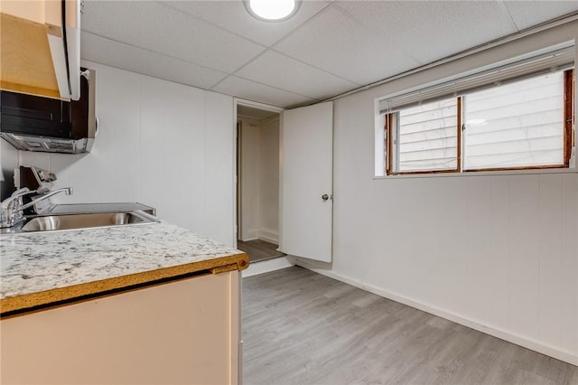 kitchen featuring light wood-style floors, a paneled ceiling, light countertops, a sink, and baseboards
