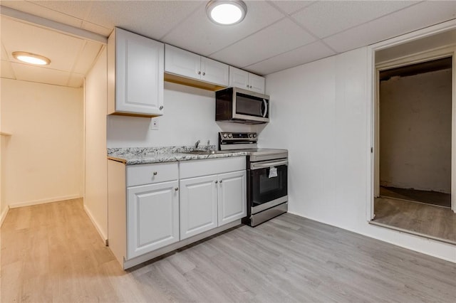kitchen with white cabinets, a sink, light wood-type flooring, a paneled ceiling, and stainless steel appliances