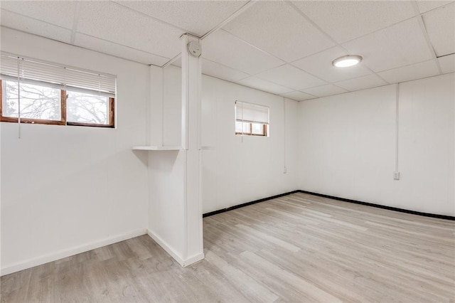 below grade area with light wood-type flooring, a paneled ceiling, and plenty of natural light