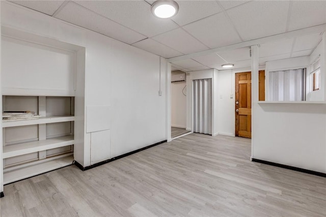 interior space with a wall mounted air conditioner, a paneled ceiling, baseboards, and wood finished floors