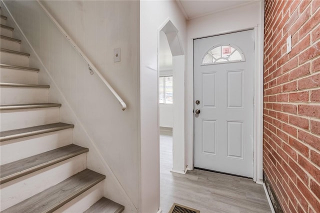 entryway featuring arched walkways, visible vents, stairway, wood finished floors, and brick wall