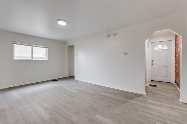 unfurnished living room featuring arched walkways, light wood-style flooring, baseboards, and visible vents