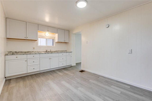 kitchen featuring baseboards, light stone counters, white cabinets, light wood-style floors, and visible vents