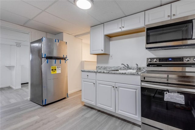 kitchen with light wood-type flooring, white cabinetry, stainless steel appliances, a drop ceiling, and a sink