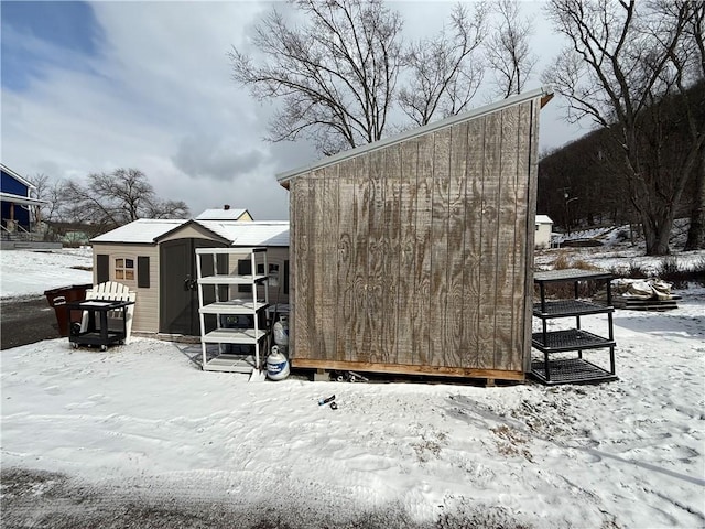 snow covered structure featuring an outbuilding and a shed