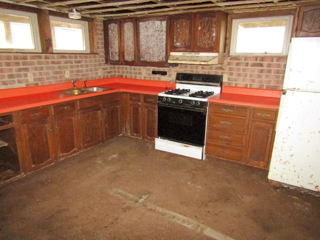 kitchen with freestanding refrigerator, ventilation hood, a sink, gas range oven, and brown cabinets