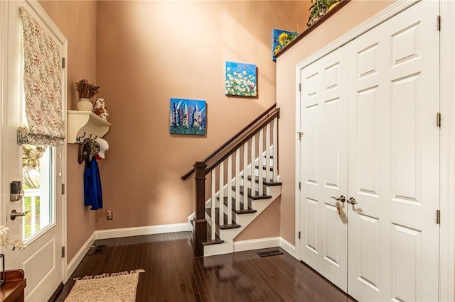 entrance foyer with dark wood-style flooring, baseboards, visible vents, and stairs
