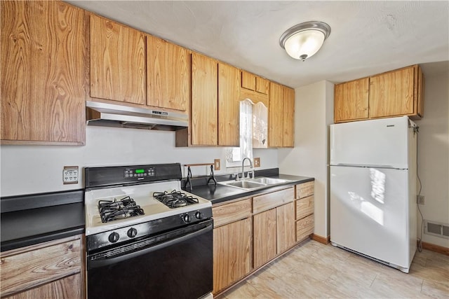 kitchen featuring visible vents, gas range, a sink, freestanding refrigerator, and under cabinet range hood