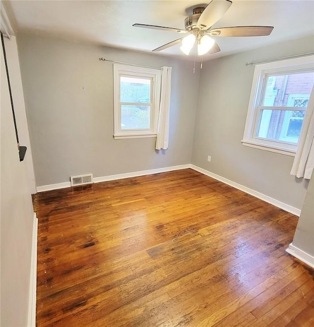 empty room with ceiling fan, baseboards, visible vents, and hardwood / wood-style flooring