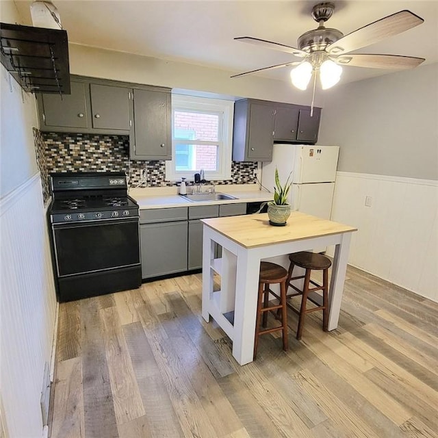 kitchen with light wood-style flooring, gray cabinetry, black range with gas stovetop, and a wainscoted wall