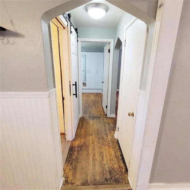 hall featuring arched walkways, a wainscoted wall, and wood finished floors