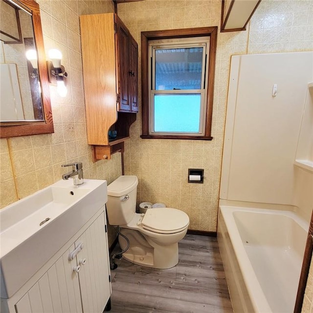 full bath with toilet, wood finished floors, vanity, and tile walls