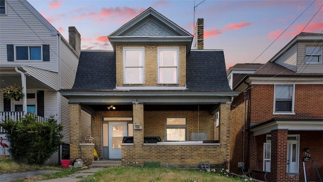 view of front of house featuring a porch, roof with shingles, and brick siding