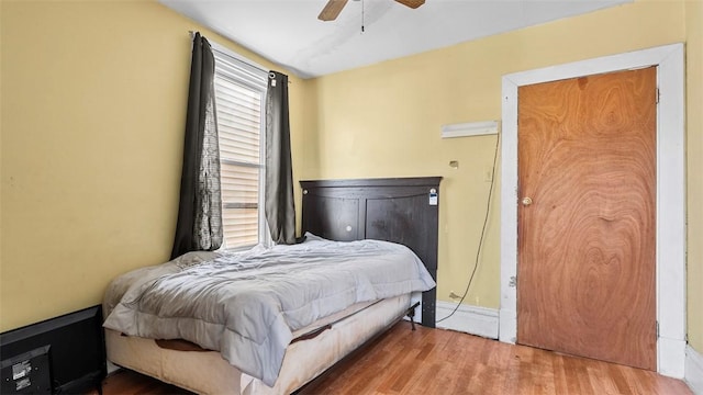 bedroom with a ceiling fan, wood finished floors, baseboards, and multiple windows