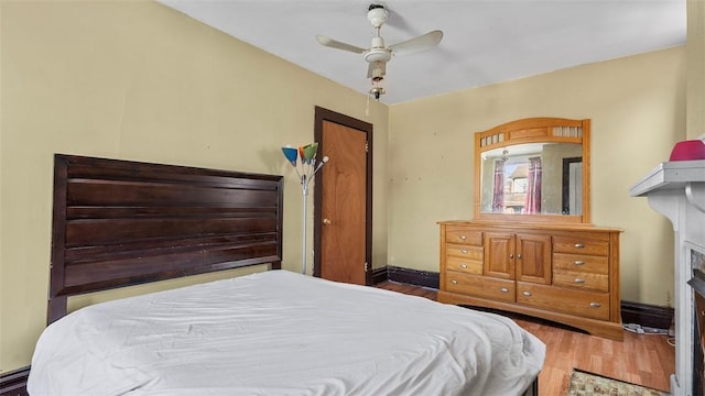 bedroom featuring baseboards, a ceiling fan, wood finished floors, and a fireplace