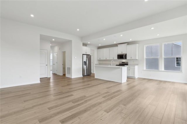 unfurnished living room with recessed lighting, a sink, light wood finished floors, and baseboards