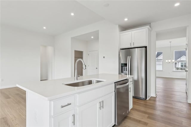 kitchen with a kitchen island with sink, appliances with stainless steel finishes, a sink, light countertops, and a chandelier