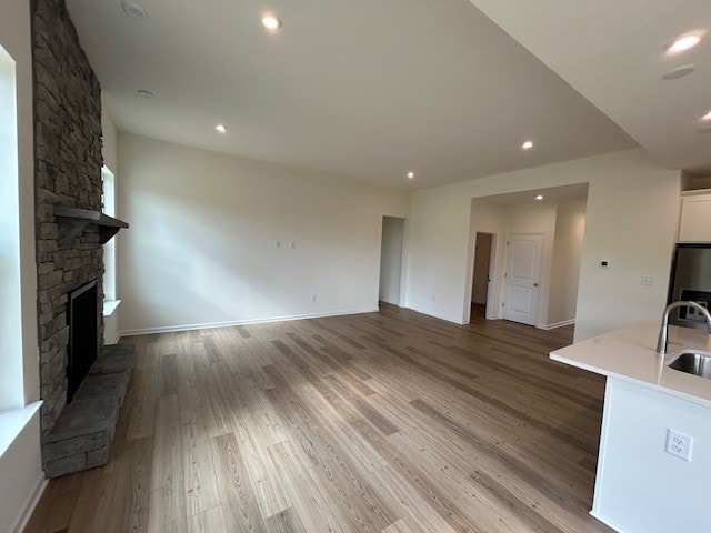 unfurnished living room featuring a large fireplace, a sink, baseboards, light wood-style floors, and recessed lighting