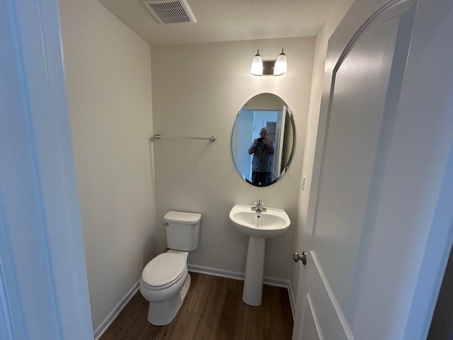 bathroom with visible vents, wood finished floors, toilet, baseboards, and a sink