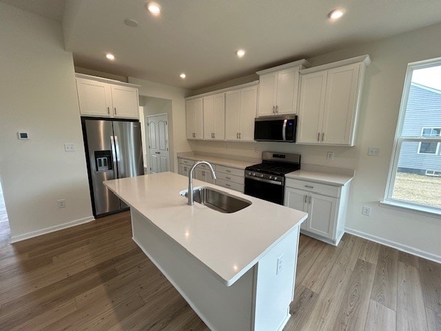 kitchen featuring a sink, light countertops, light wood finished floors, stainless steel appliances, and an island with sink