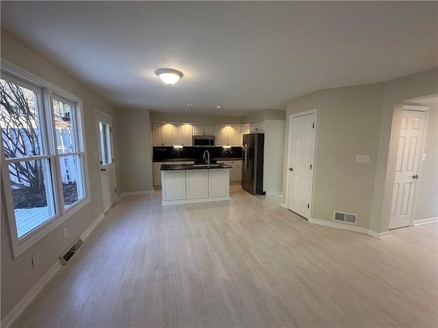 kitchen featuring a wealth of natural light, fridge with ice dispenser, stainless steel microwave, a sink, and dark countertops