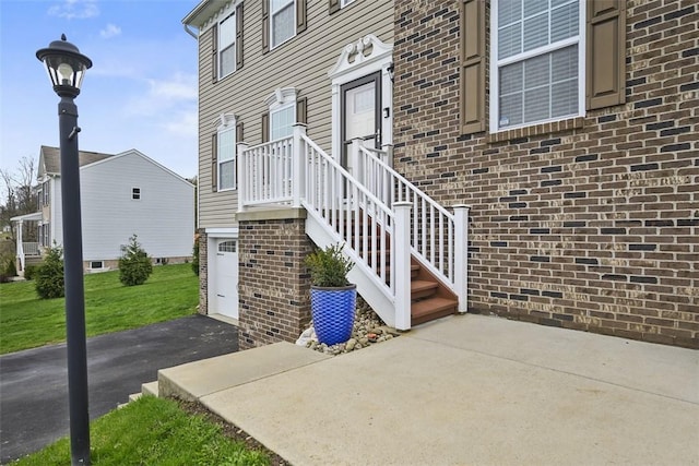doorway to property featuring a garage, aphalt driveway, brick siding, and a yard