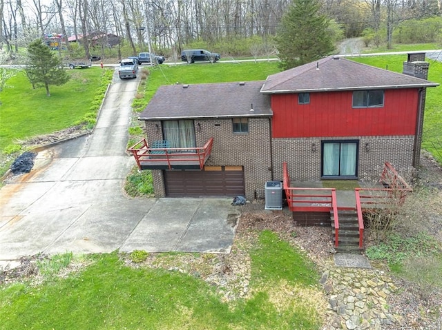 rear view of house with central AC, a lawn, a chimney, concrete driveway, and brick siding