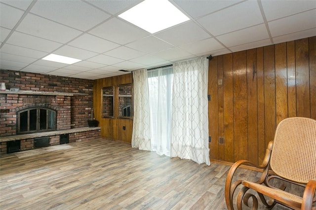 sitting room featuring a fireplace, wooden walls, light wood-style flooring, and a drop ceiling