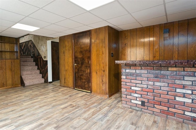 finished basement featuring wooden walls, a drop ceiling, and wood finished floors