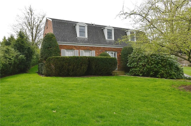 view of front facade with a gambrel roof, a shingled roof, a front lawn, and brick siding