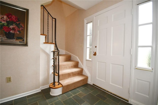 entryway with stairway, stone finish floor, and baseboards