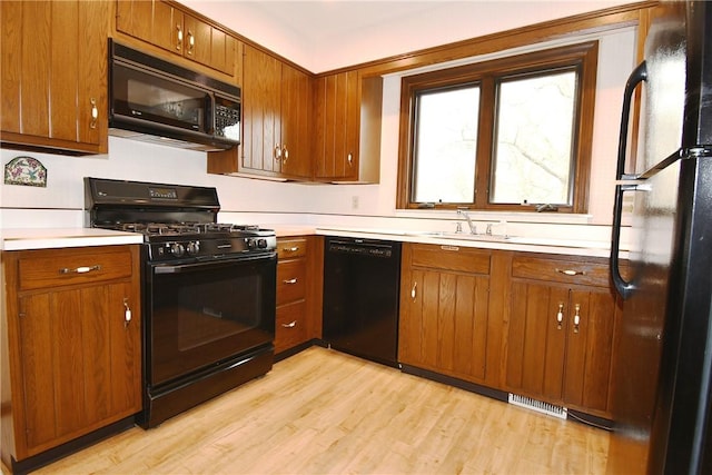 kitchen featuring light wood finished floors, brown cabinets, visible vents, and black appliances