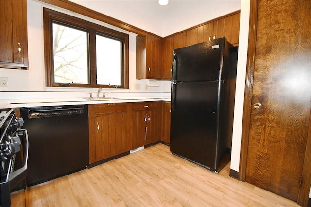 kitchen featuring light wood-type flooring, light countertops, black appliances, brown cabinets, and a sink