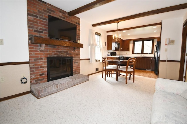 living area featuring beamed ceiling, baseboards, a chandelier, and a fireplace