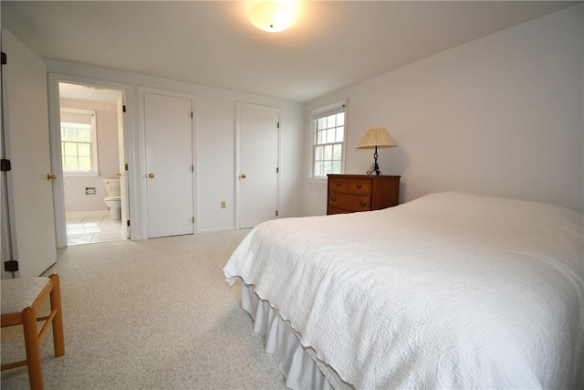 bedroom featuring multiple windows, connected bathroom, and light colored carpet