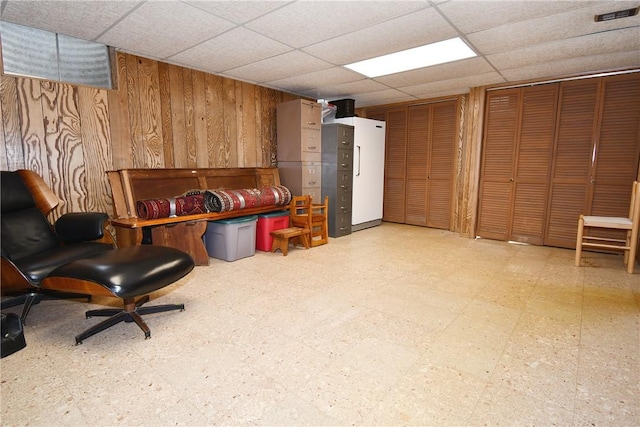 living area with wood walls, a drop ceiling, and light floors