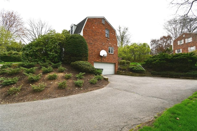 view of home's exterior featuring an attached garage, a gambrel roof, and aphalt driveway