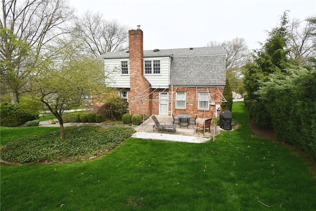 back of house with a shingled roof, a lawn, a chimney, a patio, and brick siding