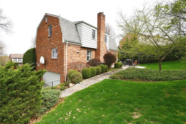 view of side of property featuring a garage, a yard, brick siding, and a gambrel roof