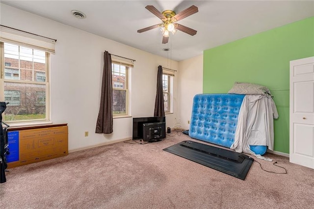 workout area with a wood stove, carpet, visible vents, and ceiling fan