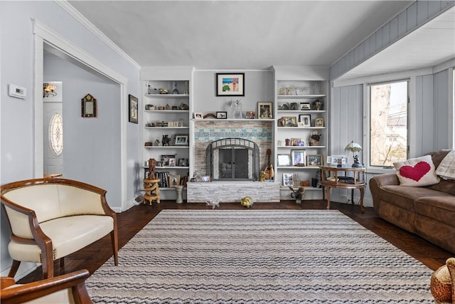 sitting room featuring built in shelves, a fireplace with raised hearth, baseboards, and ornamental molding