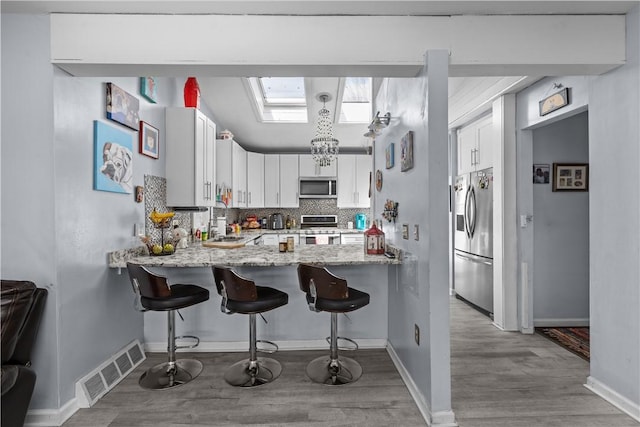 kitchen featuring visible vents, a sink, appliances with stainless steel finishes, a peninsula, and light stone counters
